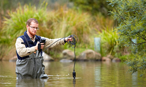 Person standing in water with measuring equipment.